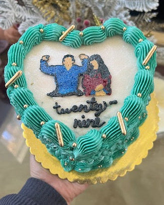 Decorative cake with a couple's silhouette and 'twenty-ninth' text, held by a person.