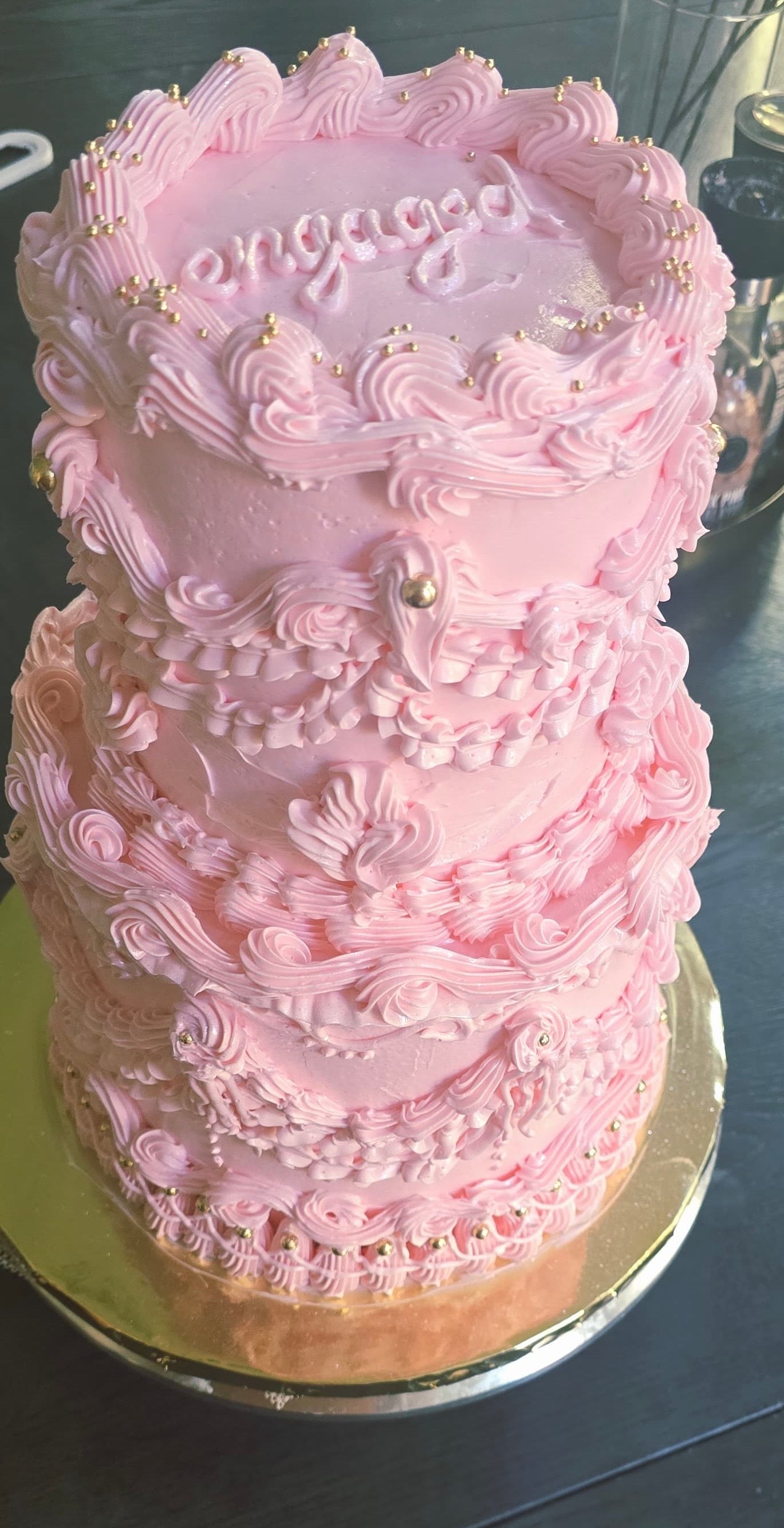 Pink decorative cake with intricate designs on a reflective surface